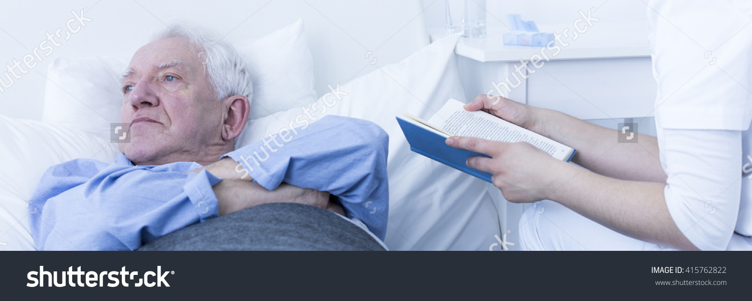 stock-photo-hospice-pensioner-lying-in-bed-caregiver-reading-book-sitting-next-to-patient-s-bed-in-light-415762822